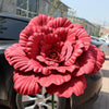 A vibrant pink artificial peony flower in full bloom displayed on a dark car.