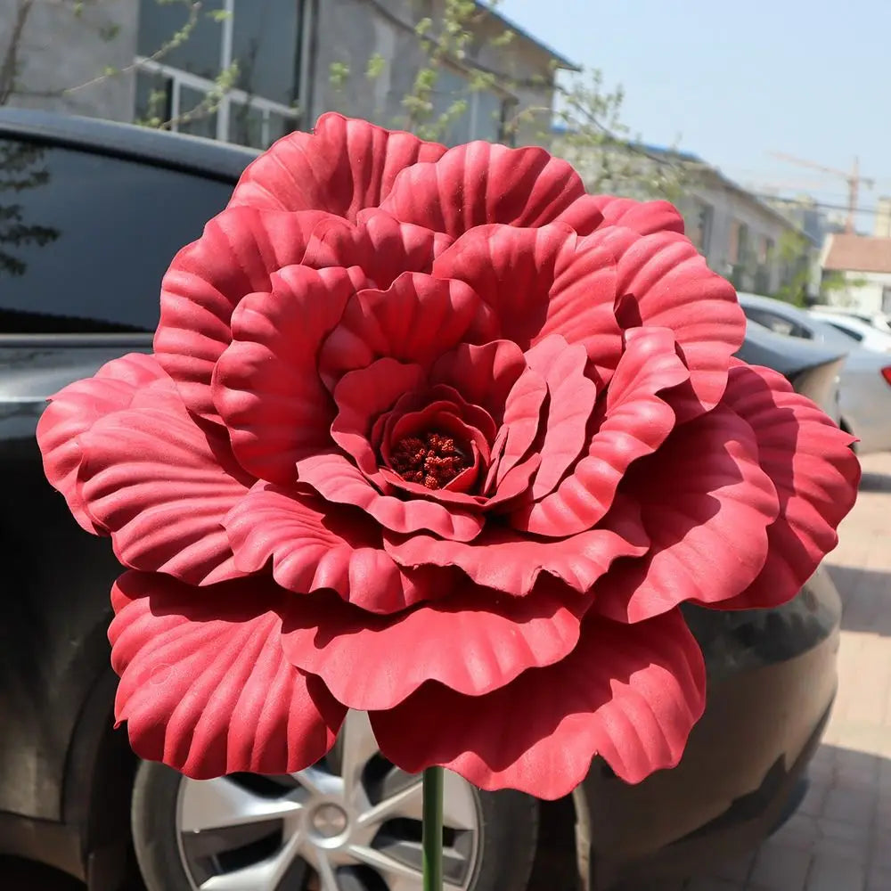 A vibrant pink artificial peony flower in full bloom displayed on a dark car.
