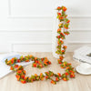 A silk rose garland with orange and yellow flowers is displayed on a white vase on a light wooden surface.