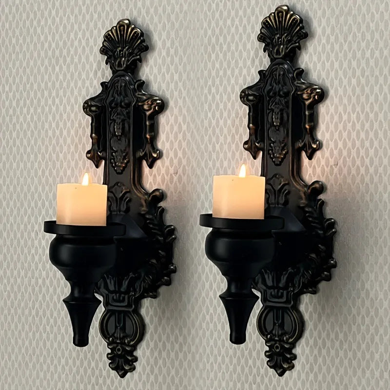A set of two vintage wrought iron wall-mounted candle holders with black bases and lit candles.