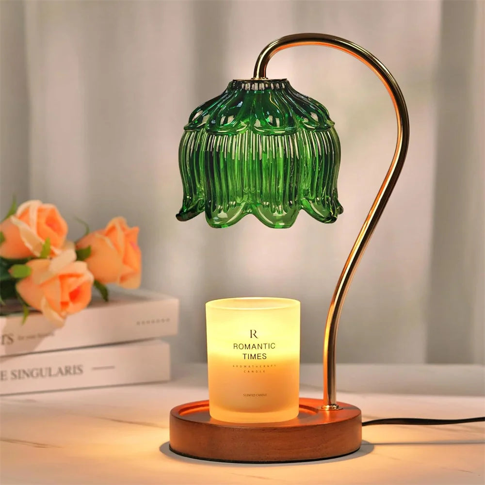 A bronze-colored lamp with a green glass petal shade illuminates a candle on a wooden base.