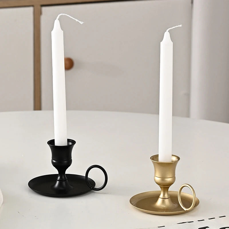 Elegant metal candle holder with a white taper candle on a white table.