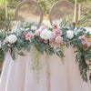 A floral garland featuring pink and white roses and green eucalyptus leaves displayed on a light pink draped table.