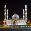 Night photo of a large Islamic mosque with prominent minarets and a dome illuminated against the dark sky.