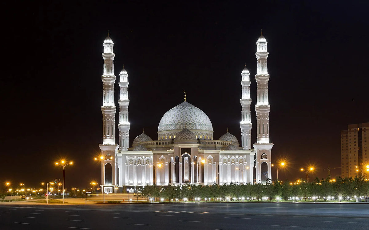 Night photo of a large Islamic mosque with prominent minarets and a dome illuminated against the dark sky.