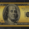 A close-up of a gold-colored United States $100 Federal Reserve Note from 1997, featuring Benjamin Franklin.