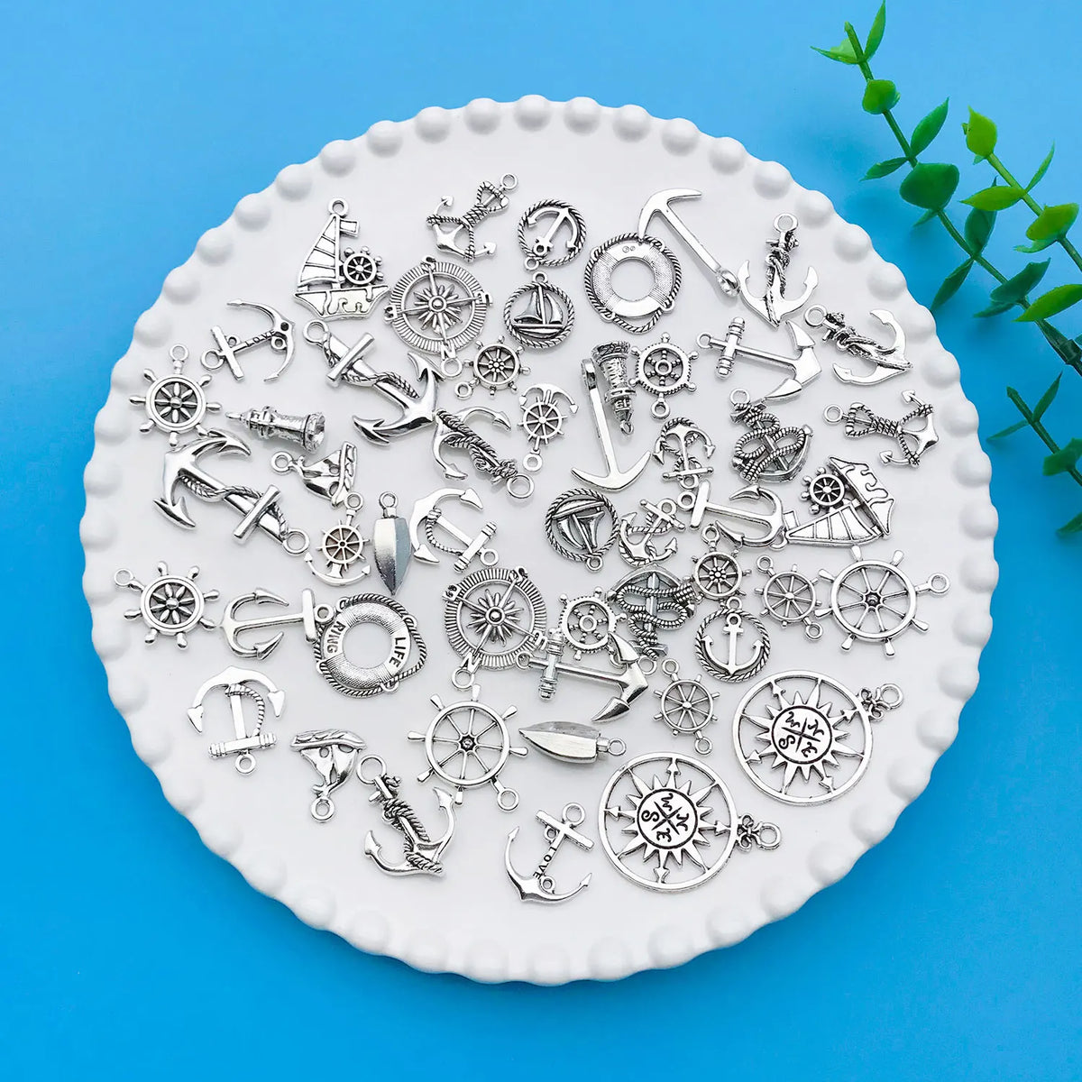 A collection of vintage ship anchor charms and nautical jewelry components displayed on a white scalloped plate.
