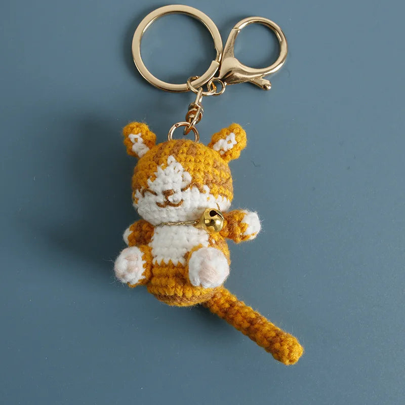Handcrafted crochet cat keychain pendant with yellow and white fur against a gray background.