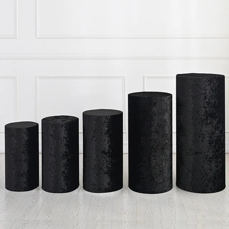 A row of black spandex cylinder stand covers, varying in height, displayed against a white paneled wall.