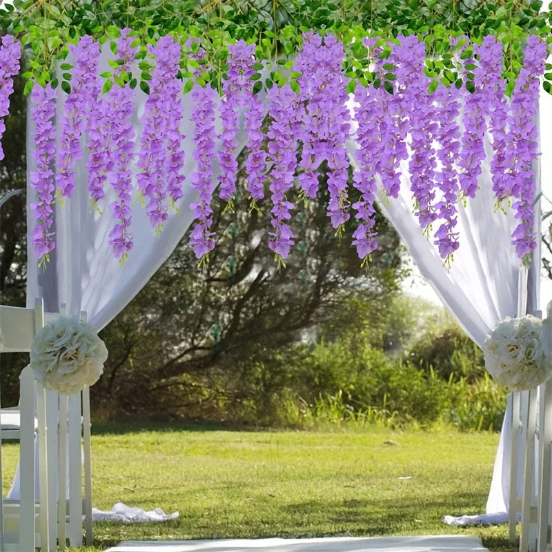 A white floral archway decorated with purple artificial wisteria vine garlands and greenery for an outdoor event.