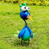 A colorful garden sculpture of a peacock with large eyes and bright blue and green feathers standing on green grass.