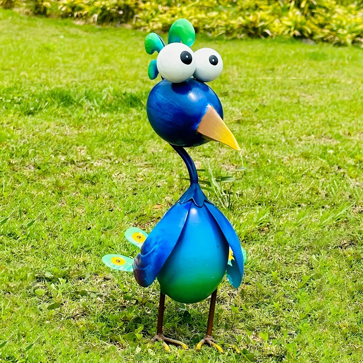 A colorful garden sculpture of a peacock with large eyes and bright blue and green feathers standing on green grass.