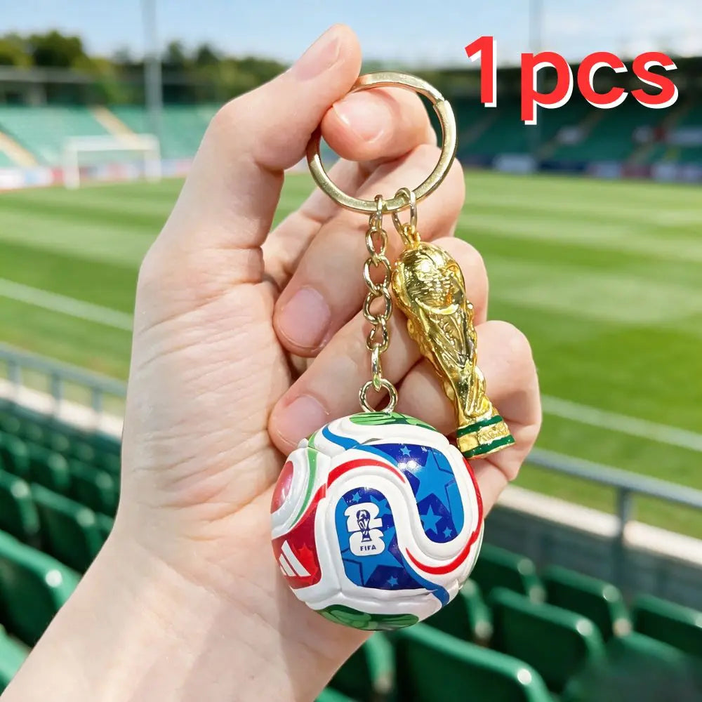 A hand holds a FIFA trophy keychain featuring a soccer ball and a golden eagle charm.