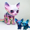 A pink and purple articulated 3D printed Siamese cat figurine with large, iridescent eyes.