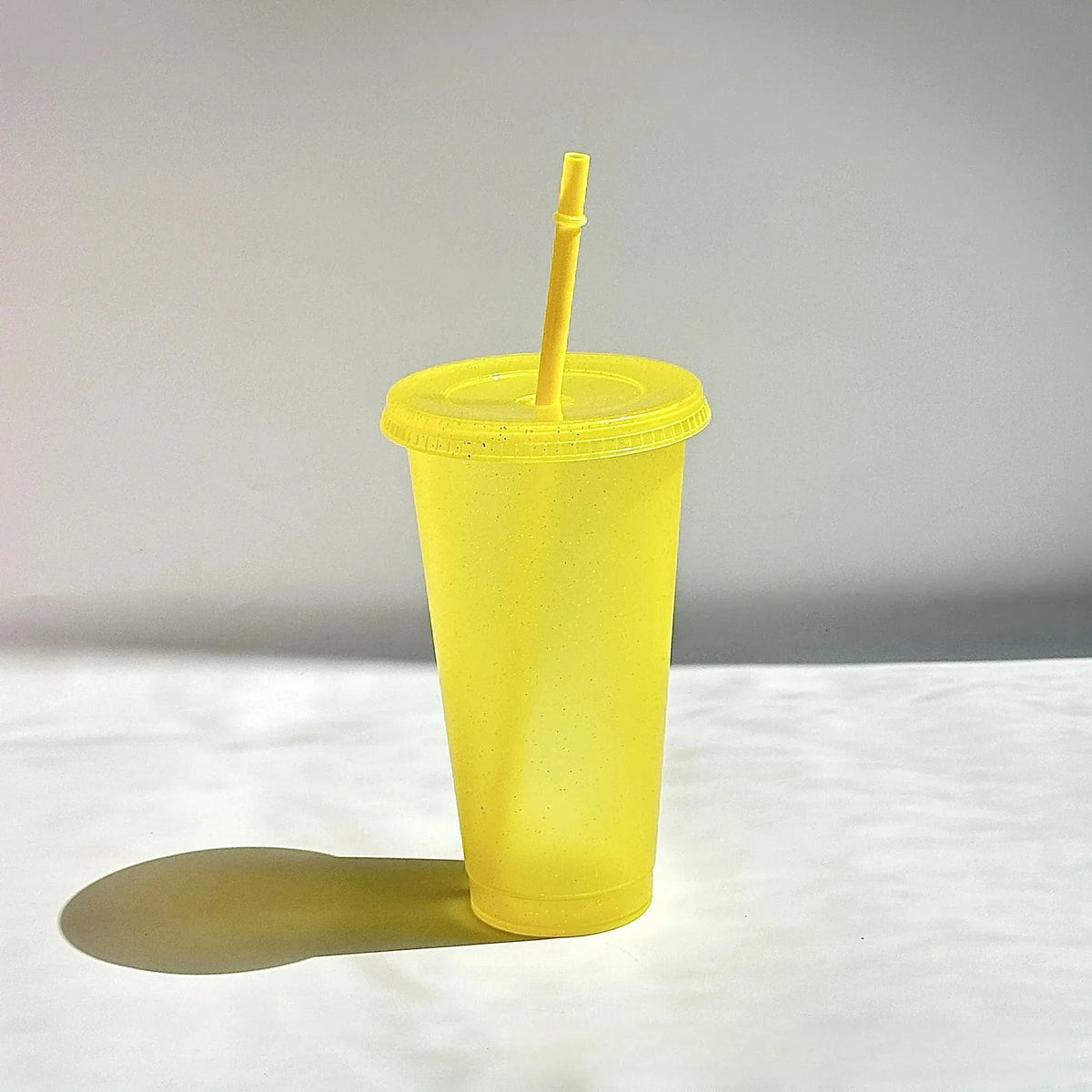 A yellow glitter party cup with a straw is shown against a white background.
