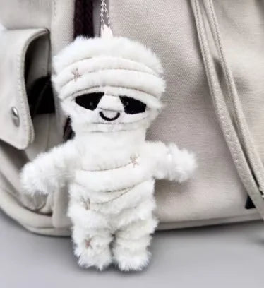 A white mummy skeleton plush keychain is hanging from a strap against a light beige fabric background.
