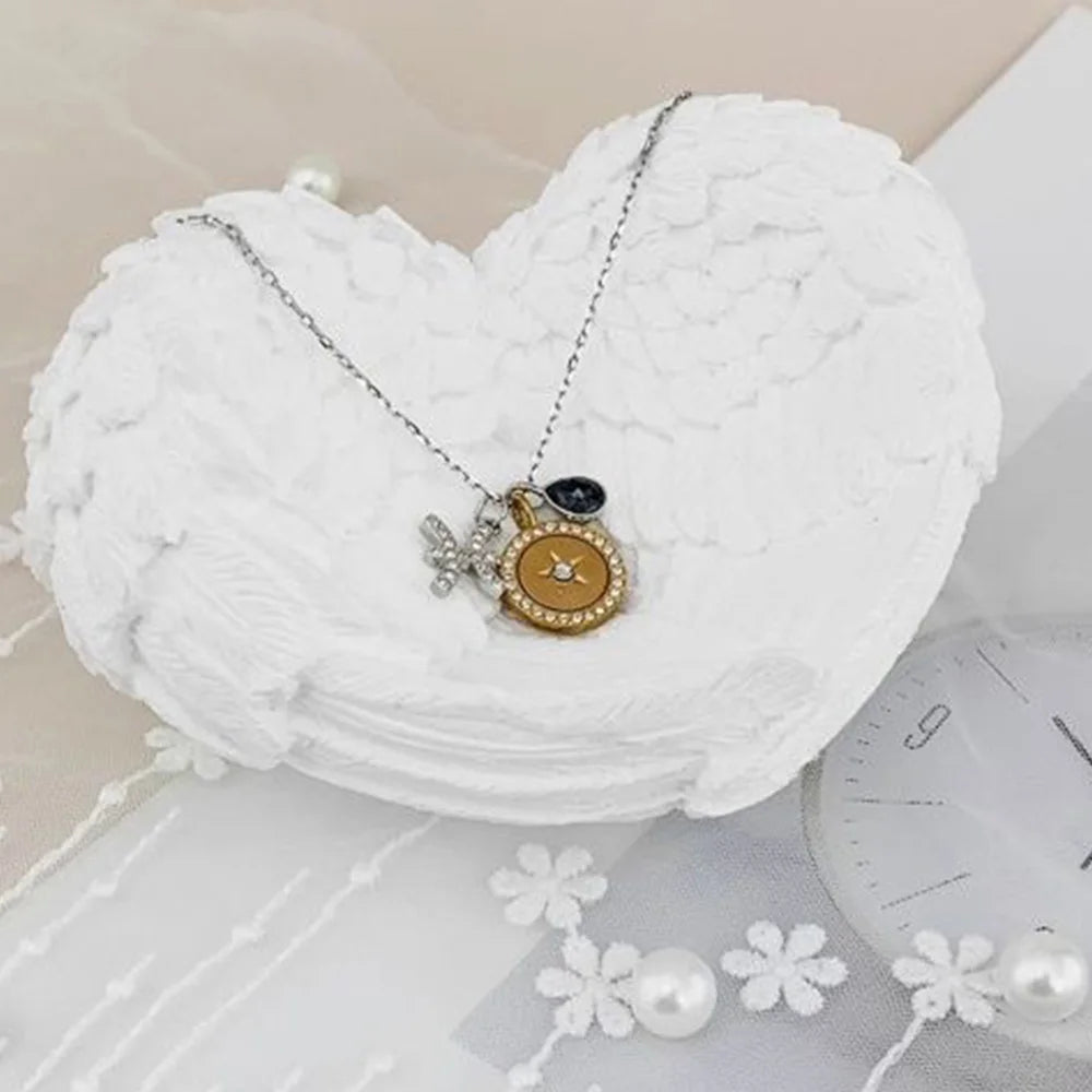 Silver necklace with angel wings and a dark stone pendant resting on a white heart-shaped fabric.