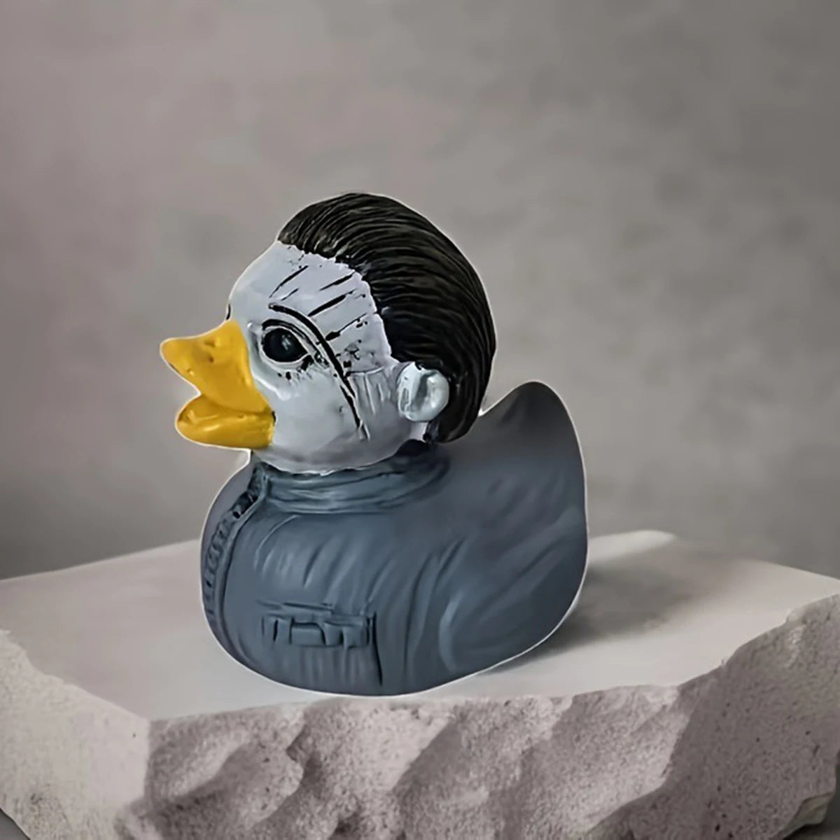 A ceramic figurine of a duck with a stylized, distressed face and gray body, displayed on a white surface.