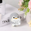 A gray crocheted penguin plush sits next to a white card with an encouraging message on a white surface.