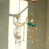 Gold moon-shaped crystal suncatcher with iridescent teal and blue crystals hanging from a branch.