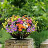 A vibrant bouquet of silk daisies in various colors like purple, orange, and yellow, displayed on a stone pedestal.