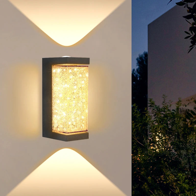 An outdoor wall sconce featuring a rectangular crystal light encased in a dark finish, illuminated by upward-pointing light b