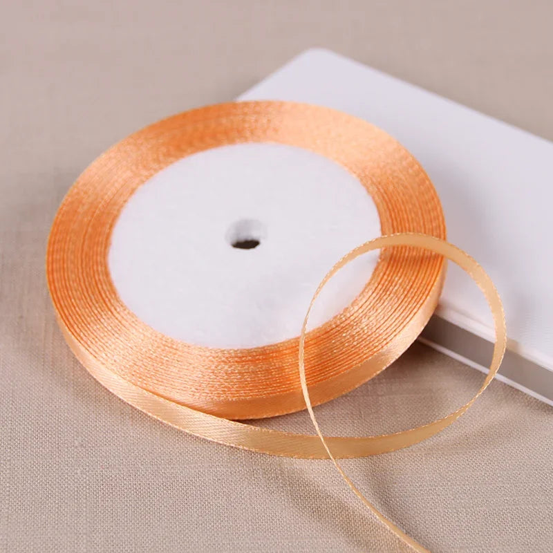 A spool of orange satin ribbon lying on a light beige surface.