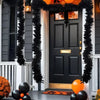 A black door decorated with a shimmering tinsel ribbon garland and orange accents for holiday decor.