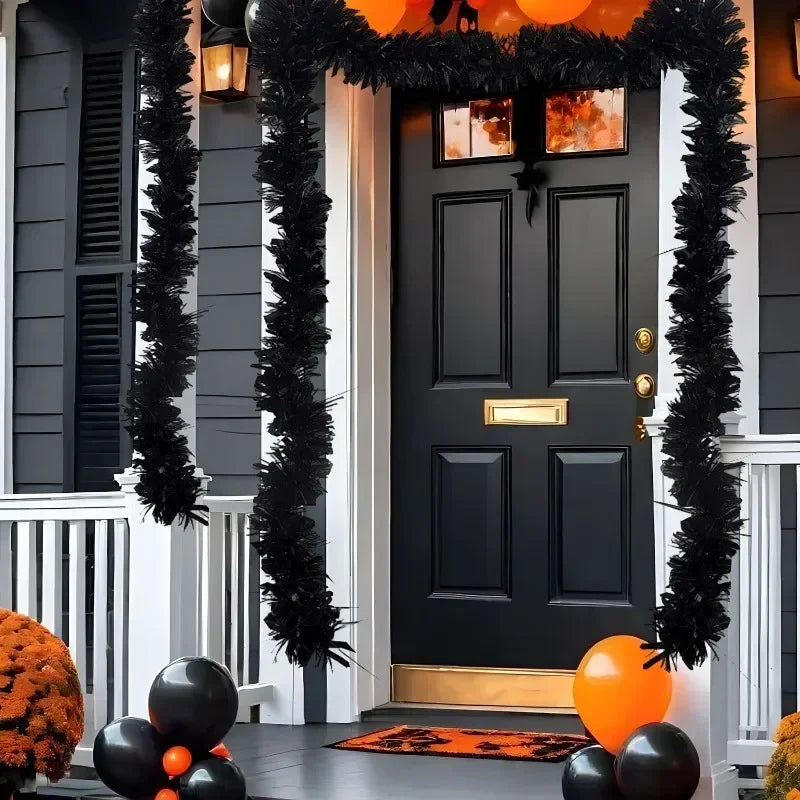 A black door decorated with a shimmering tinsel ribbon garland and orange accents for holiday decor.