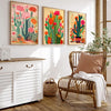 A set of three framed posters featuring colorful vintage cactus and floral art displayed on a white shelf.