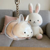 A clear acrylic rabbit charm keychain hangs against a soft gray sofa with a white stuffed rabbit.