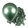 A single shiny metallic green latex balloon resting on a pile of crumpled green foil balloons.