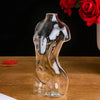 An artistic glass vase shaped like a human body, filled with amber-colored liquid, set against a dark background.