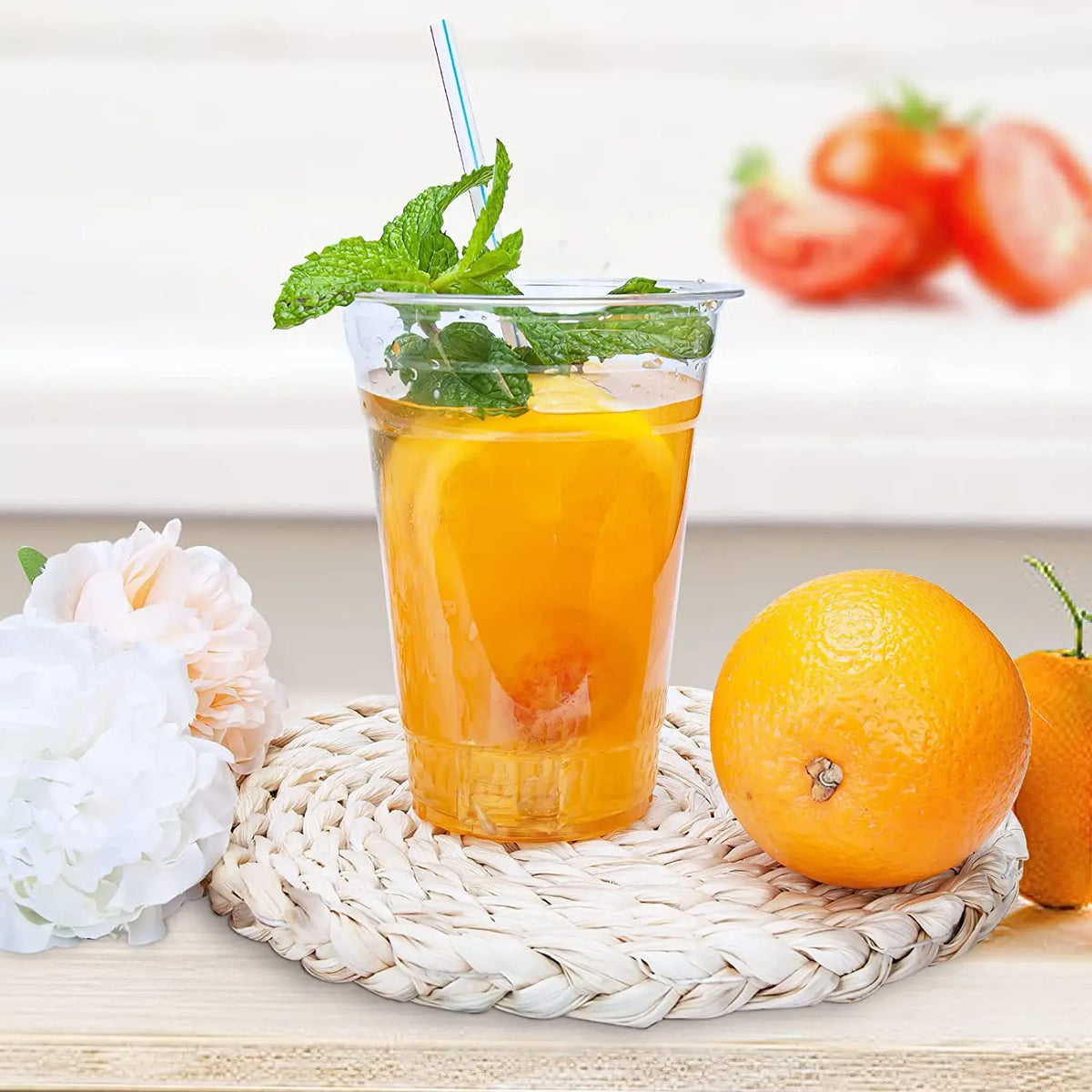 A glass of orange juice garnished with mint on a woven coaster next to a whole orange.