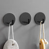 Three black stainless steel self-adhesive wall hooks with natural twine hangers mounted on a gray wall.