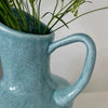 A light blue speckled ceramic pitcher holding green foliage.