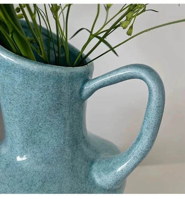 A light blue speckled ceramic pitcher holding green foliage.