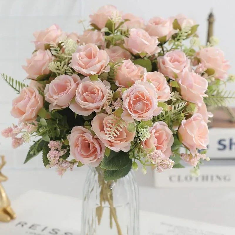 A bouquet of pink and peach artificial roses with green foliage displayed in a glass vase.