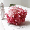 A pink silk hydrangea stem with vintage burnt edge petals displayed next to a white figurine.