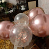 A collection of rose gold foil balloons, including clear and pink shades with rose gold confetti, used for birthday decor.