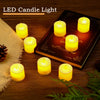 A set of glowing yellow LED candle lights placed on a wooden surface next to pine cones and green foliage.