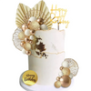 A white cake decorated with gold and champagne-colored spherical toppers and a gold birthday banner.