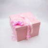 A pink gift box tied with a sheer pink ribbon and gold accents, presented against a white background.