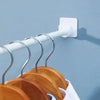 White adjustable self-adhesive curtain rod brackets mounted on a wall, holding wooden hangers.