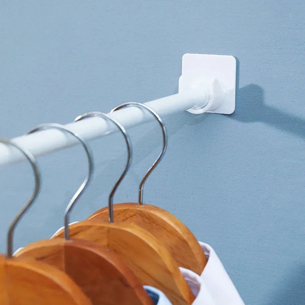 White adjustable self-adhesive curtain rod brackets mounted on a wall, holding wooden hangers.