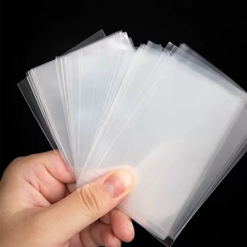 A hand holds a stack of clear card sleeves protector pack for display or protection.