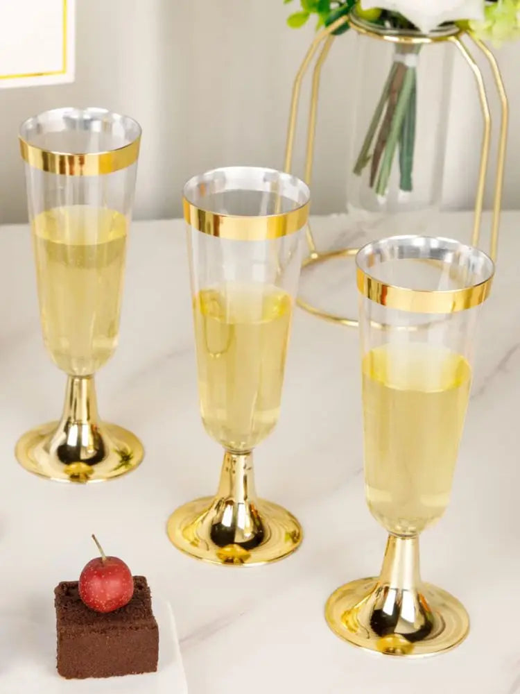 Three elegant gold-rimmed champagne flutes filled with pale yellow liquid on a white surface.