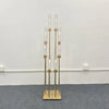 A tall gold metal candelabra set featuring eight glass candle holders displayed against a white wall.