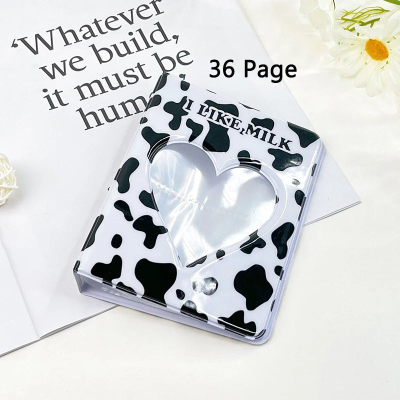 A clear heart-shaped photo album cover with a black and white cow print design resting on a white background.