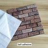 A rectangular self-adhesive 3D brick pattern wall sticker with brown and gray tones placed on a wooden surface.